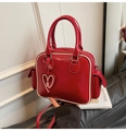 Detail of red patent leather Boston bag featuring heart pendant and white piped edges - Red & White