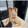 Detailaufnahme einer Stroh-Handytasche mit braunem Lederbesatz und modischem Etikett - Cremeweiß