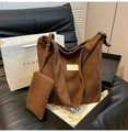 Detail of dark brown corduroy tote bag and matching mini pouch on a black sofa - Brown