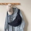 Minimalist black crescent crossbody bag in nylon shown hanging over a denim jacket - Black