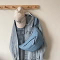 Light blue crescent crossbody bag in nylon shown on a casual denim jacket outfit - Blue