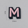 Écusson brodé lettre M rose sur tissu noir, dimensions de 4 cm de haut et 3,8 cm de large - Lettre M
