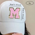 Detail view of pink towel embroidered M letter patch on white cotton baseball cap - Letter M / Pink / Hot Melt Adhesive