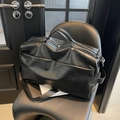 Close-up of the black leather travel tote bag with silver zippers on a chair - Black