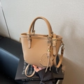 Beige lychee pattern bucket bag with small dog charm on designer books background - Khaki
