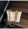 Detail of a white bucket tote with brown leather straps and a plush bear charm on books - With Charm / Off White