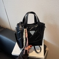 Black quilted handbag with silver triangular logo and braided rope detail on a display book - Black with Pendant