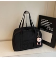 Close-up of black nylon travel tote with pink plush charm on a minimal white surface - With Charm / Black