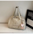 Close-up of beige canvas travel bag with front zipper pocket and plush monster charm - With Charm / Off White