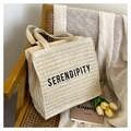 Stroh-Tote-Tasche in Hafergelb mit Serendipity-Stickerei auf einem Holzstuhl - Weiß