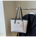 Detail of grey woven tote bag featuring black leather trim and decorative metallic charms - With Pendant / Gray