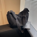 Sac hobo moderne en denim noir délavé avec large bandoulière posé sur un canapé - Noir