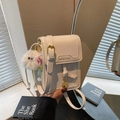Beige square phone bag with gold buckle and plush charm in a lifestyle setting - With Charm / White