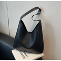 Dettaglio di una borsa tote nera minimalista in pelle opaca appoggiata su un libro - Nero