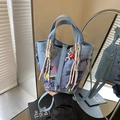 Bolso tipo cubo de mezclilla azul con grafitis y colgantes, de mano mostrado por modelo - Con Colgante / Azul