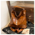 Close-up of brown vintage leather tote bag showing glossy texture and front pocket details - Caramel color