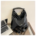 Detail of black glossy crinkled leather tote bag showing shiny texture on glass desk - Black