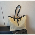 Close-up of woven straw tote bag featuring black leather trim and decorative buckle detail - Black