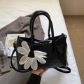 Black leather bucket bag with woven texture and a large white floral accent piece - Black