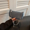 Blaue Denim Satteltasche mit silbernen Nieten und Kettenriemen in der Hand - Hellblau