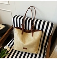Détail d'un sac cabas en paille tissée avec anses en cuir brun sur une chaise - Marron
