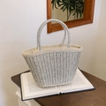 Silver woven straw tote bag with metallic handles placed on a vintage book - Silver