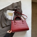 Details der roten Handtasche mit Krokodilprägung, Rundgriffen und Metallstandfüßen - Rotes Steinmuster