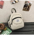 Detail of a minimalist beige mini backpack with a square fabric label on the front pocket - White