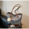 Detail of blue denim tote bag with brown leather trim and plush charm on a book - Blue (With Charm)