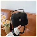 Close-up of black leather crossbody bag with silver logo and top handle on sofa - Black