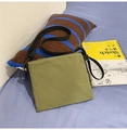 Detail of green nylon envelope bag with adjustable black strap on a cozy bedding setup - Army Green