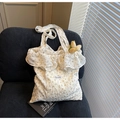 Detalle del bolso tote de flores blancas con volantes y etiqueta Magic Pocket en un sofá - Blanco Roto