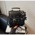 Detail eines schwarzen Kunstleder Rucksacks mit weißen Nähten und Bärenanhänger auf Box - Schwarz mit Anhänger