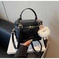 Detail der schwarzen Kastenhandtasche mit goldenem Logo und weißem Plüschtier-Anhänger - Schwarz mit Anhänger