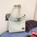 Borsa tote in nylon verde chiaro con coulisse e tracolla regolabile su un letto - verde chiaro