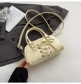 Detail view of cream Boston bag with cross-lace design and metallic eyelets on white surface - Yellow
