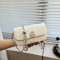 Bolso de hombro minimalista crema con cadena plateada y cierre de metal sostenido en la mano - Caqui