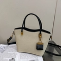 Close-up of beige textured tote bag featuring black leather handles and a mini gold pendant - Cream & Black