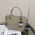 Detailopname van beige rieten draagtas met lichtblauwe lederen hengsels en mini-bedeltje - Crème & Grijs