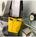 Detail of a bright yellow nylon crossbody bag featuring dual front pockets and black straps - Yellow