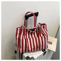 Bolso tote de lona a rayas rojas y blancas con asas de cuero sobre una maleta plateada - Rojo