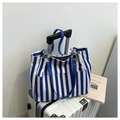 Bolso tote de lona a rayas azules y blancas con asas de cuero sobre una maleta - Azul