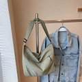 Borsa a tracolla verde chiaro in nylon con tracolla regolabile appesa accanto a un jeans - Verde