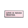 Detailed shot of pink enamel brooch with Love Is Never Wasted slogan and black metal frame - Pink Rectangle (Love)