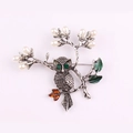 Vue macro d'une broche hibou avec yeux en cristal vert, perles blanches et feuilles - Argent antique