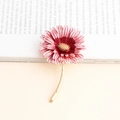 Dettaglio della spilla a margherita in smalto rosa con stelo dorato su un libro - Rosso Anguria