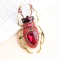 Vintage beetle brooch with red crystals and gold finish on an open book background - Red
