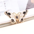 Vintage gouden vlinderbroche met witte emaille vleugels en sprankelende strassteentjes - donkergrijs