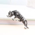 Tiger-Brosche in Silberoptik mit schwarzen Emaille-Streifen kriechend auf einem Buch - Silber