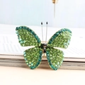 Broche papillon dorée avec strass vert dégradé posée sur les pages d'un livre ouvert - Vert